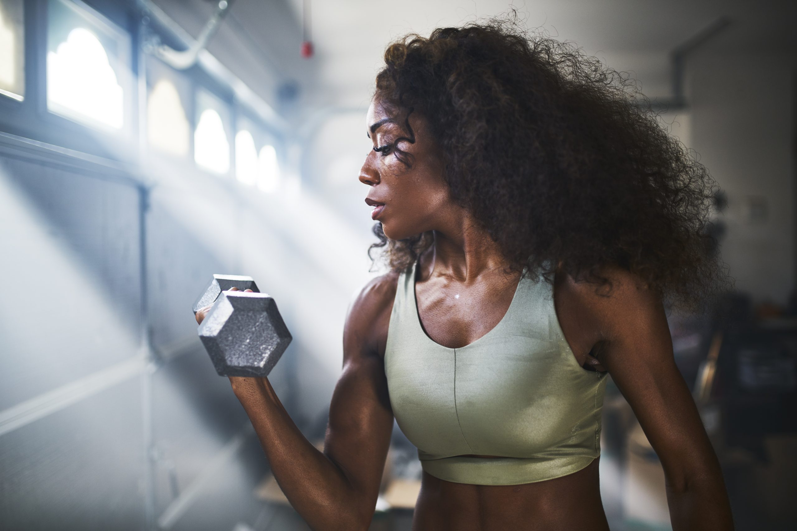 fit african american woman working out by lifting weights in home gym