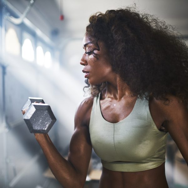 fit african american woman working out by lifting weights in home gym