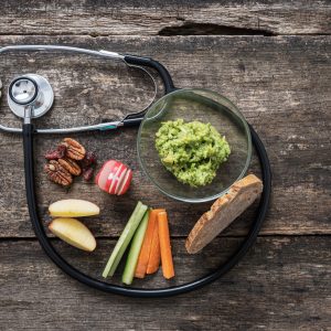Medical stethoscope making a loop around a healthy vegan snack of avocado spread, home made sourdough bread and fresh veggies. Over rustic wooden background.