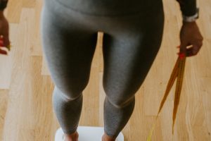 Woman Measuring Body Weight At Home. . Close up of a woman legs measuring weight with scale at home and holding measuring tape. Weight management.